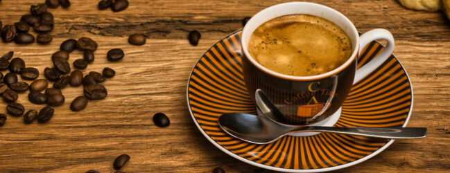 Tasse mit Espresso auf einem Tisch umgeben von Kaffeebohnen.