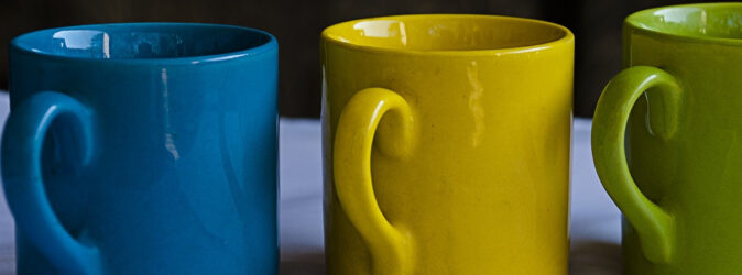 Drei leere Kaffeetassen in verschiedenen Farben nebeneinander.