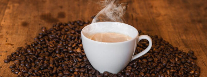 Dampfende Kaffeetasse auf einem Berg aus Kaffeebohnen.